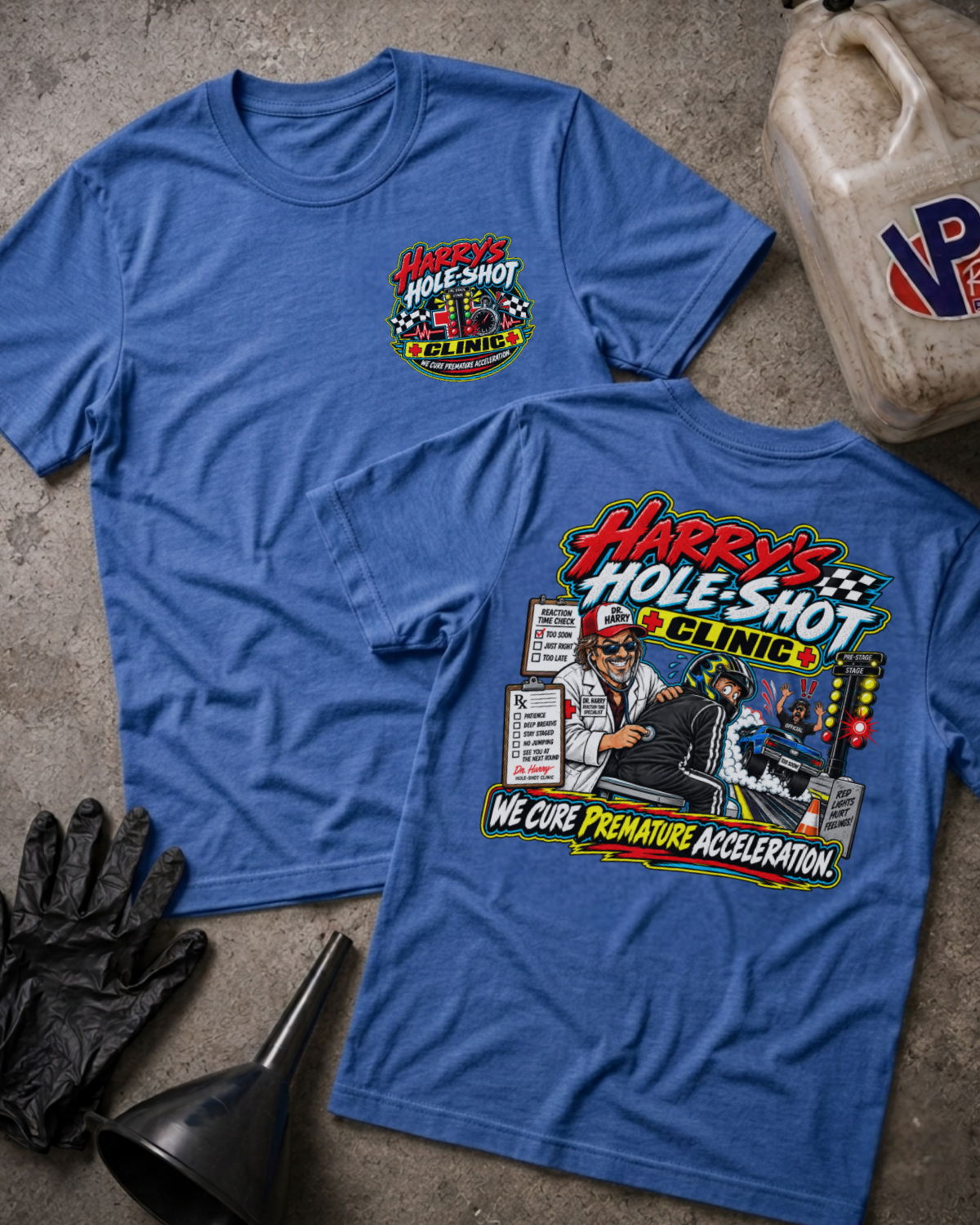Two heather blue graphic T-shirts laid flat on a concrete-like surface, showing both front and back designs. The shirts feature a colorful 'Harry's Hole-Shot Clinic' racing-themed print.