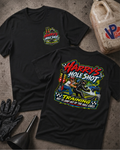 Two black graphic t-shirts displayed flat on a textured gray surface, with a black glove and funnel nearby and a plastic jug in the background. The front shirt shows a small multicolor chest graphic reading 'Harry's Hole Shot', while the back shirt shows a large colorful graphic with the text 'Harry's Hole Shot' and 'Training Not To Jump Out Of The Hole Early' and a racing scene.