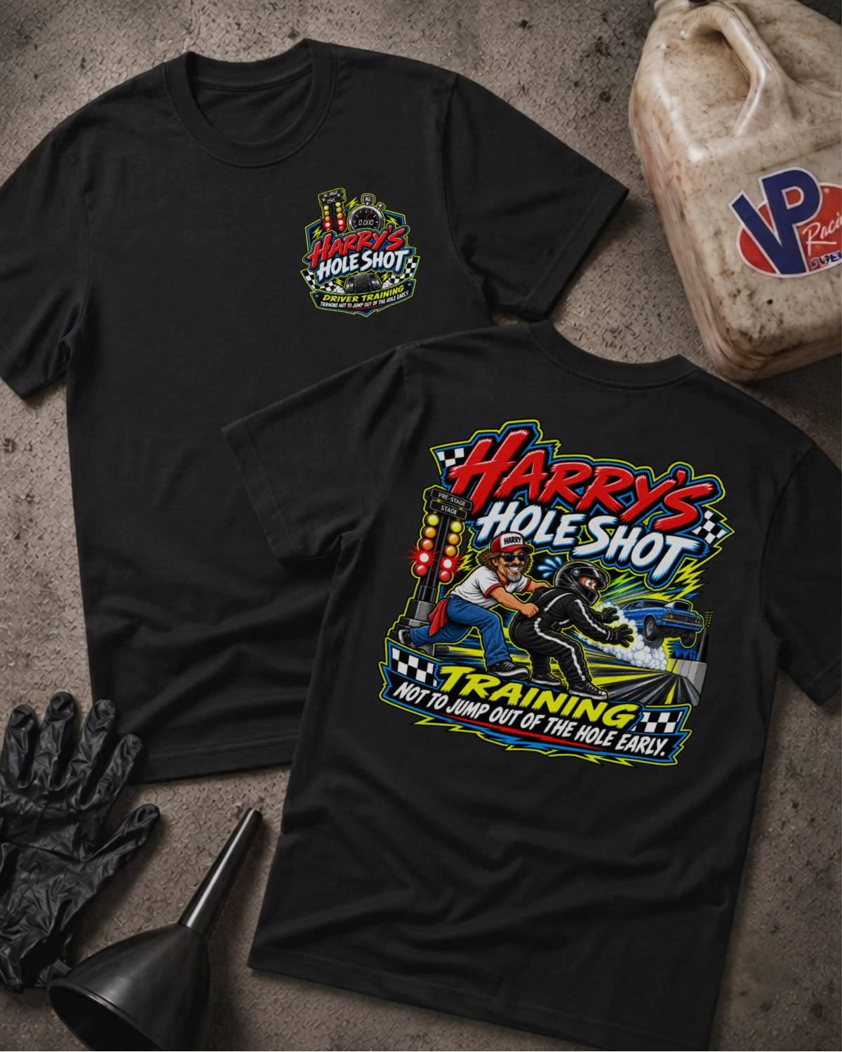 Two black graphic t-shirts displayed flat on a textured gray surface, with a black glove and funnel nearby and a plastic jug in the background. The front shirt shows a small multicolor chest graphic reading 'Harry's Hole Shot', while the back shirt shows a large colorful graphic with the text 'Harry's Hole Shot' and 'Training Not To Jump Out Of The Hole Early' and a racing scene.