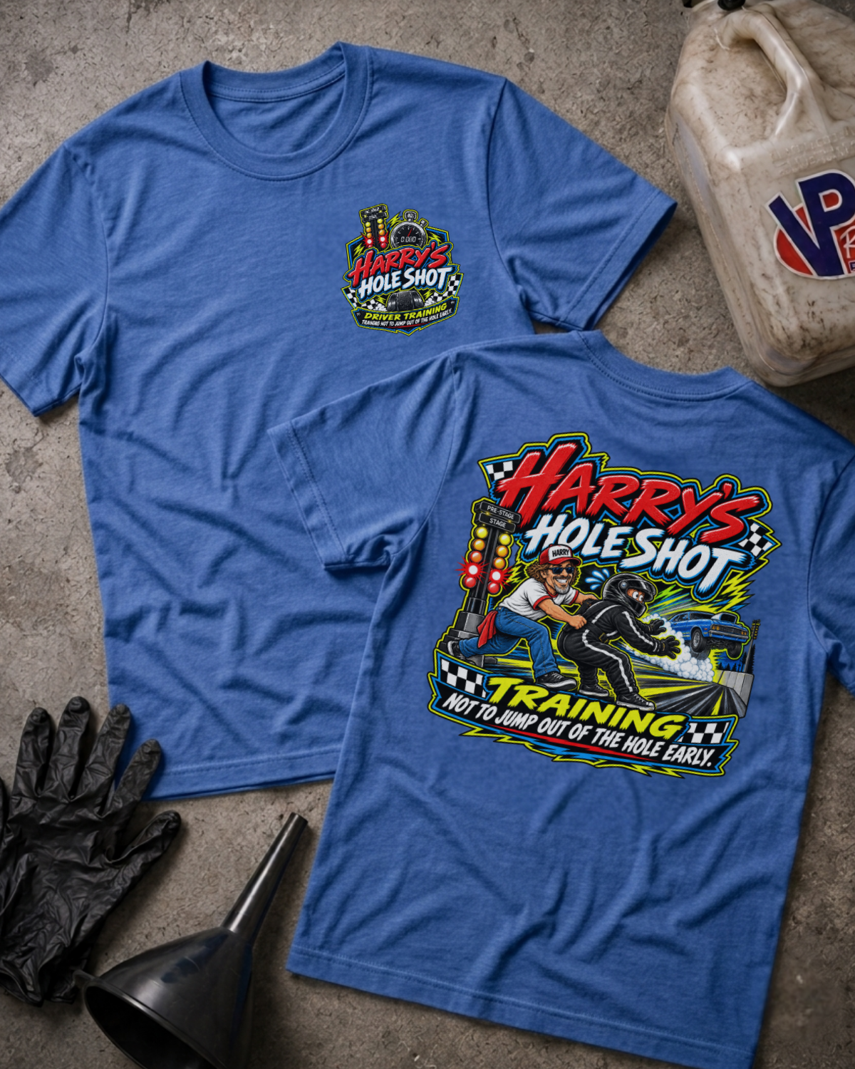 Two heather blue graphic T-shirts laid flat on a concrete surface, showing the front and back designs for 'Harry's Hole Shot'. The front features a small chest graphic, while the back has a large colorful graphic with a race car, a person, and bold text.
