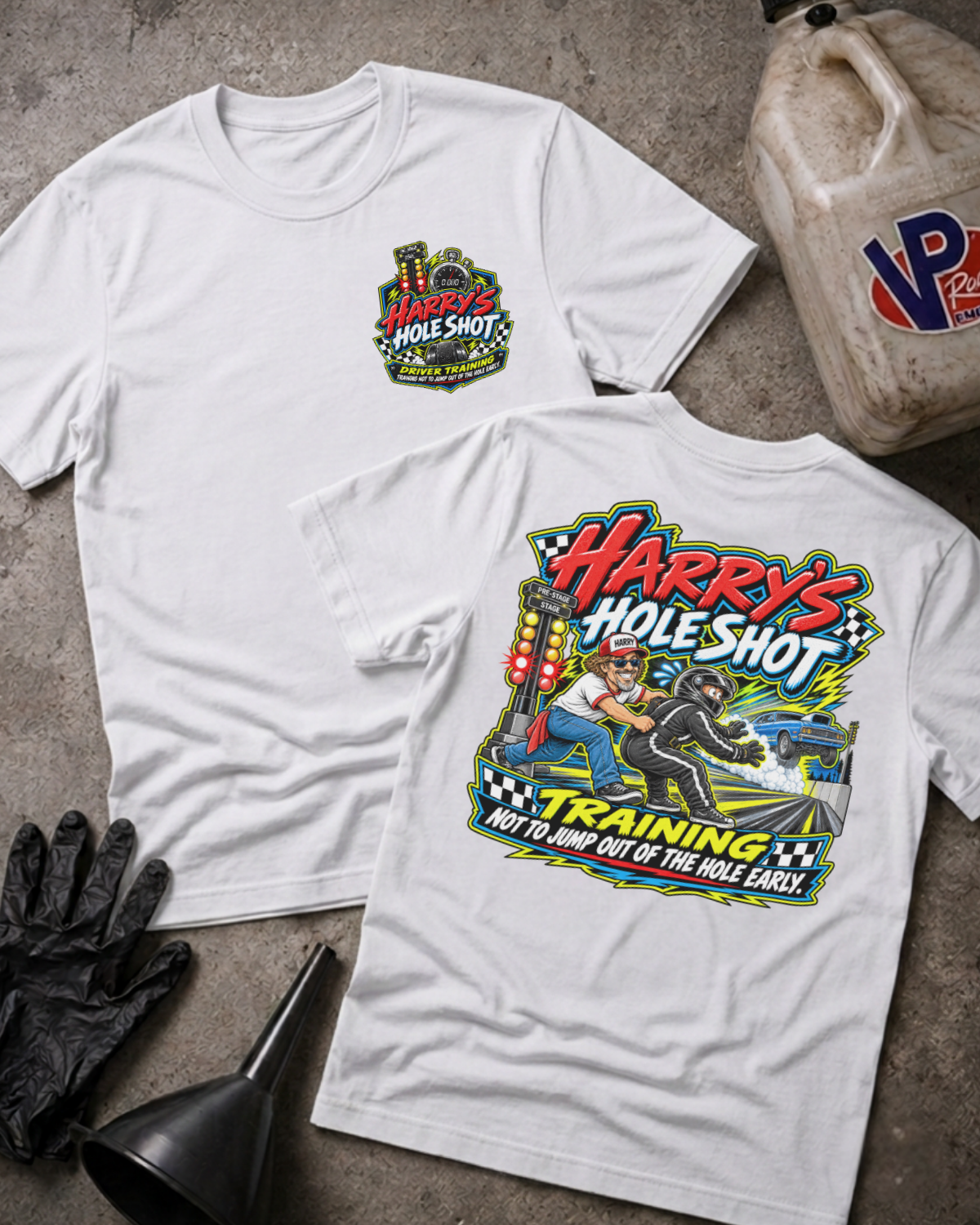 Two white graphic T-shirts displayed on a concrete surface, with a black oil jug, black gloves, and a funnel as props. The front shirt shows a small multicolor chest graphic reading 'Harry's Hole Shot,' and the back shirt shows a large colorful racing-style graphic with the text 'Harry's Hole Shot' and 'Training Not to Jump Out of the Hole Early.