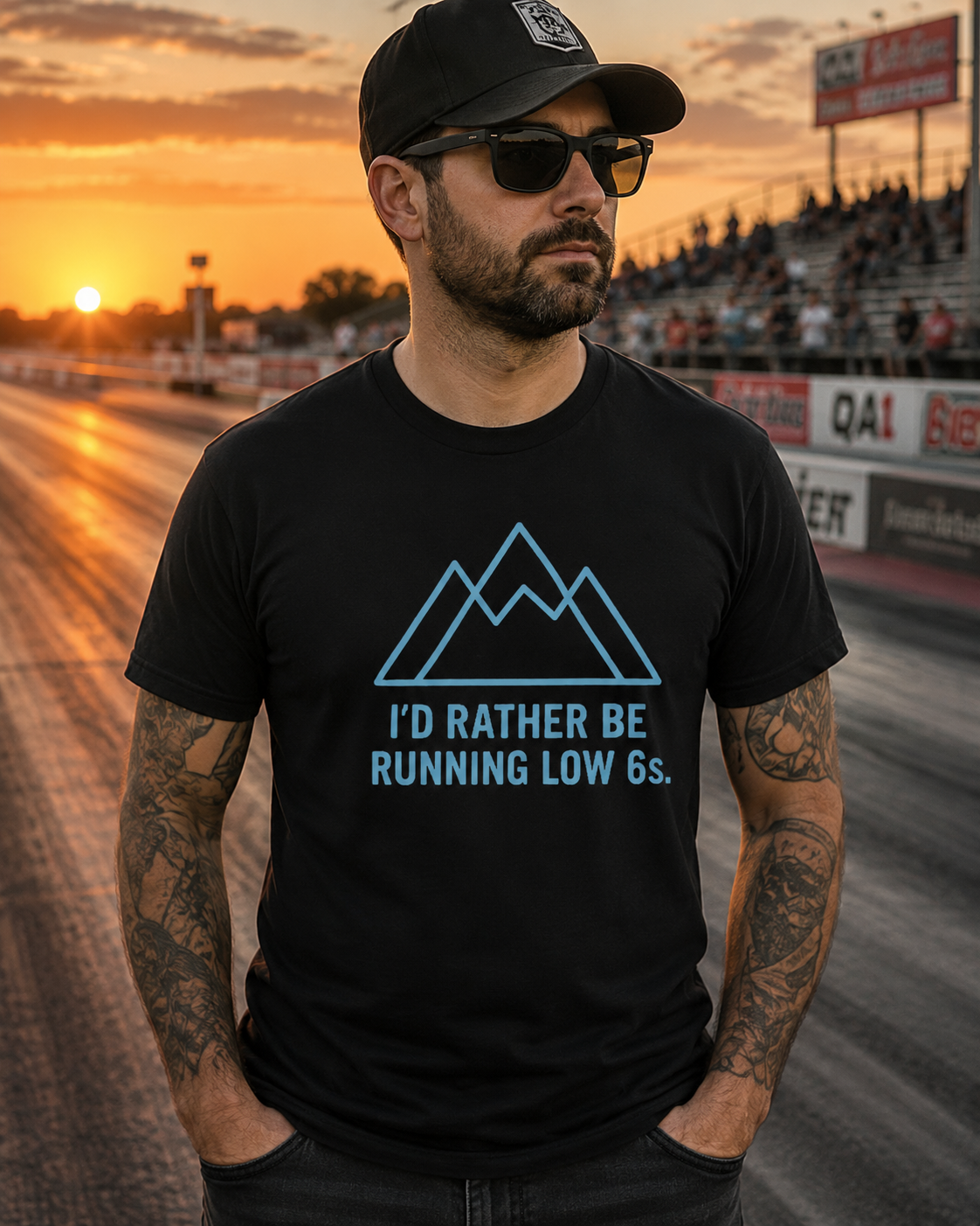 Man wearing a black t-shirt with a graphic design and text 'I'd Rather Be Running Low 6s' standing on a drag strip at sunset