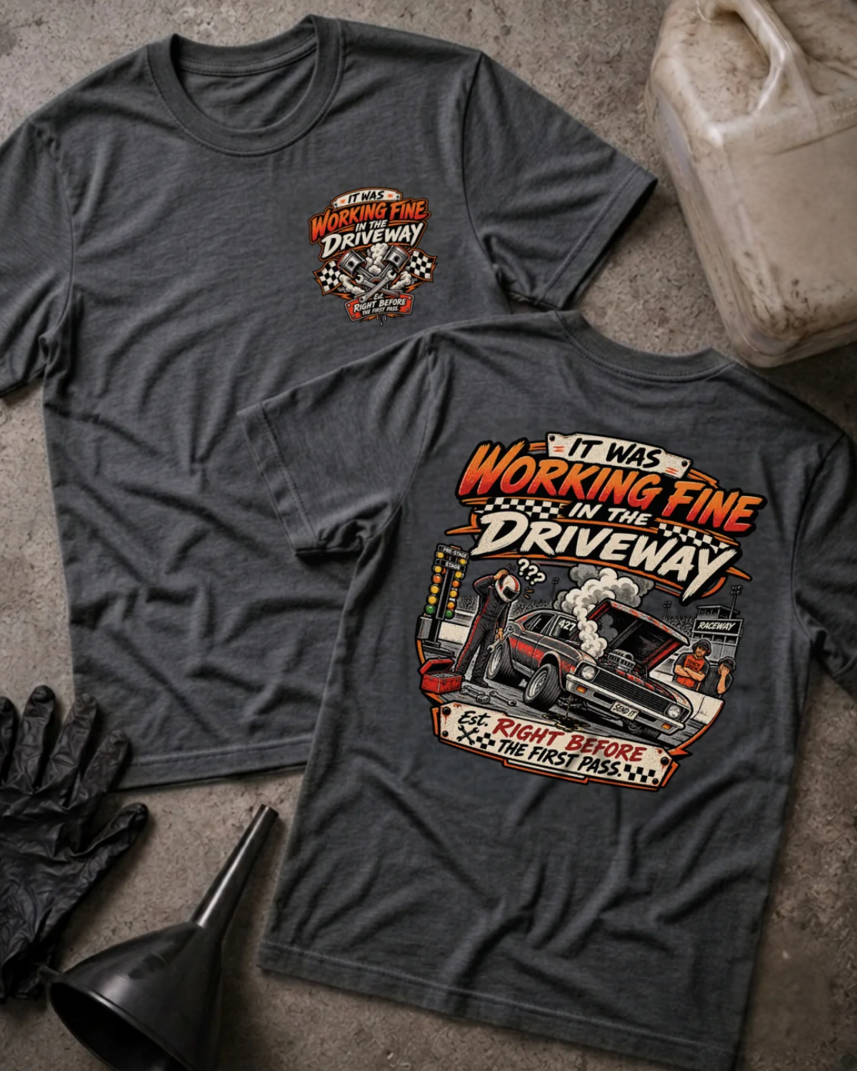Front and back of It Was Working Fine in the Driveway dark grey heather T-shirt with chest logo, smoking muscle car with open hood at a drag strip, and “Right before the first pass” text.