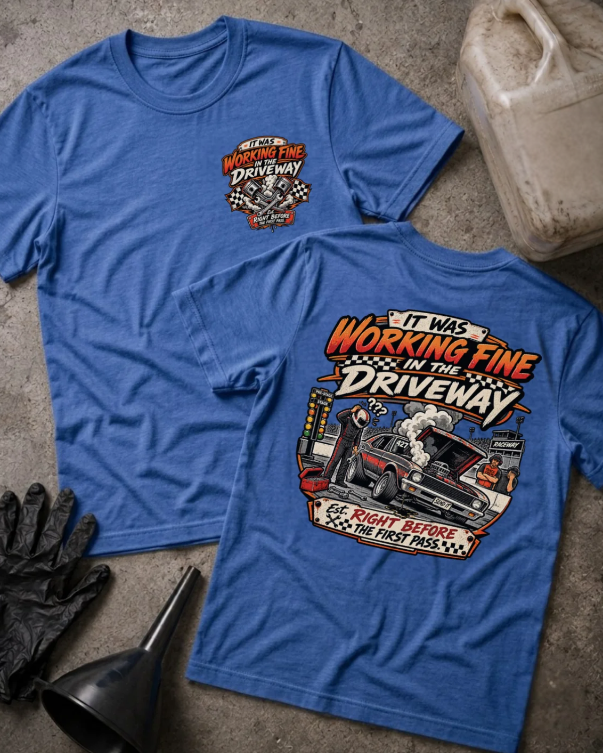 Front and back of It Was Working Fine in the Driveway heather true royal T-shirt with chest logo, smoking muscle car with open hood at a drag strip, and “Right before the first pass” text.