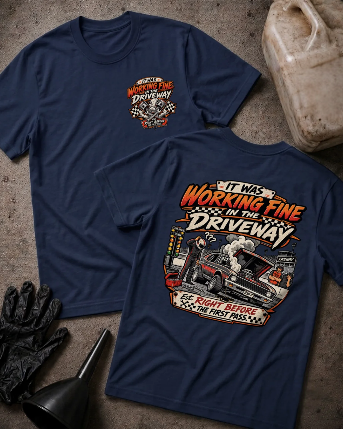 Front and back of It Was Working Fine in the Driveway navy T-shirt with chest logo, smoking muscle car with open hood at a drag strip, and “Right before the first pass” text.