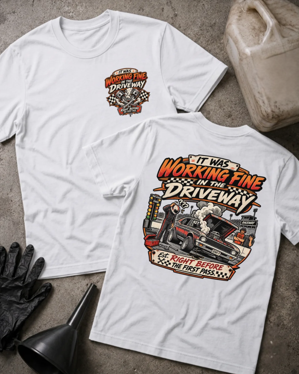 Front and back of It Was Working Fine in the Driveway white T-shirt with chest logo, smoking muscle car with open hood at a drag strip, and “Right before the first pass” text.