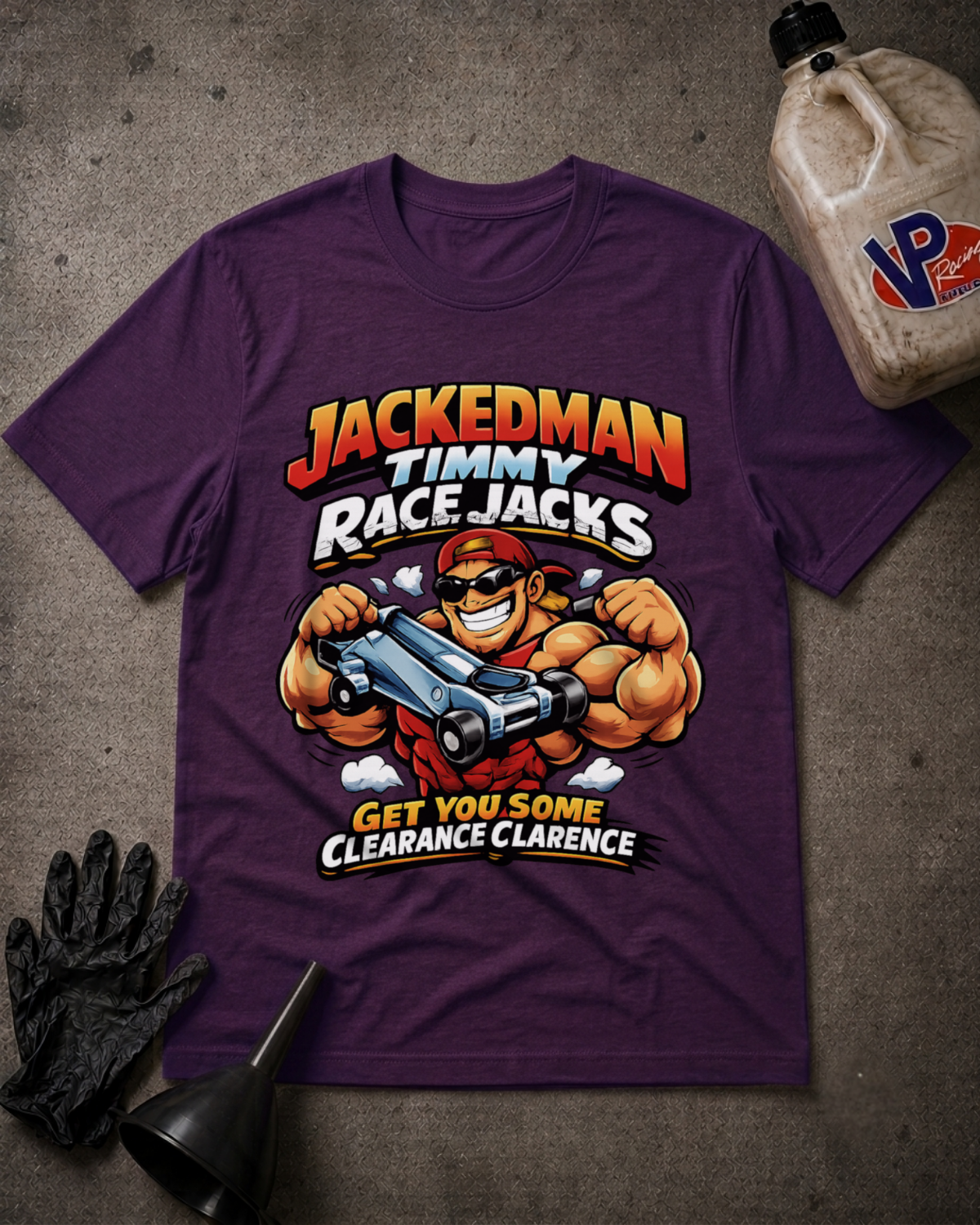 A purple graphic t-shirt featuring a cartoon illustration of a muscular race car driver named Jackedman Timmy, styled in a flat-lay with a black glove, funnel, and a bottle of oil on a gray concrete background.