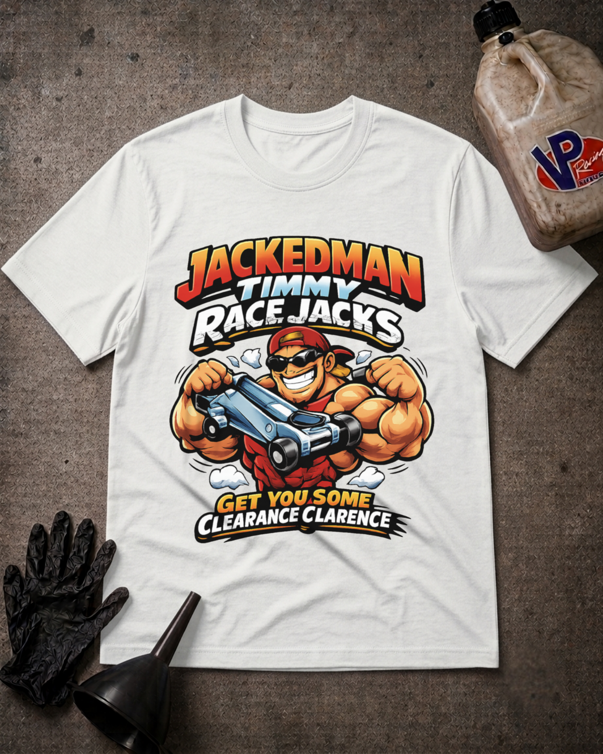 A white graphic t-shirt featuring a cartoon illustration of a muscular race car driver with the text 'JACKEDMAN TIMMY RACE JACKS' and 'GET YOU SOME CLARANCE CLARENCE'. The shirt is displayed in a flat-lay arrangement on a dark textured surface, accompanied by a black oil glove, a black funnel, and a plastic jug of VP Racing Oil.