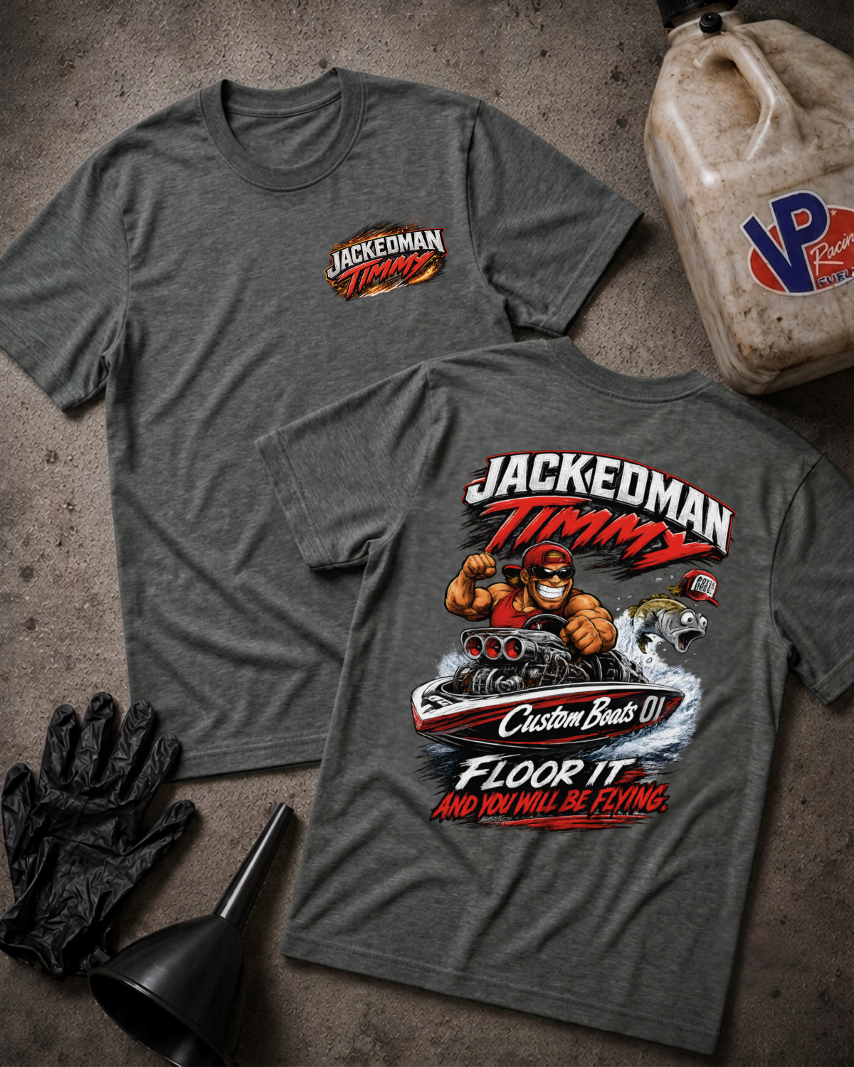 Two heather dark gray graphic T-shirts laid flat on a textured concrete-like surface, with a black funnel, black gloves, and a dirty plastic jug as styling props. The front shirt shows a small 'Jackedman Timmy' chest graphic, and the back shirt shows a large multicolor graphic with the same brand text and an illustrated figure.