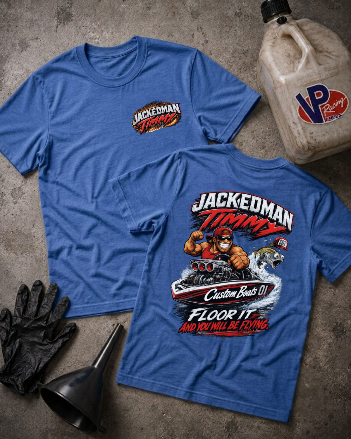Two blue graphic T-shirts laid flat on a concrete surface, showing the front and back designs. The front has a small 'JACKEDMAN TIMMY' chest logo, and the back has a large multicolor racing graphic with 'JACKEDMAN TIMMY' and 'FLOOR IT AND YOU WILL BE FLYING' text.