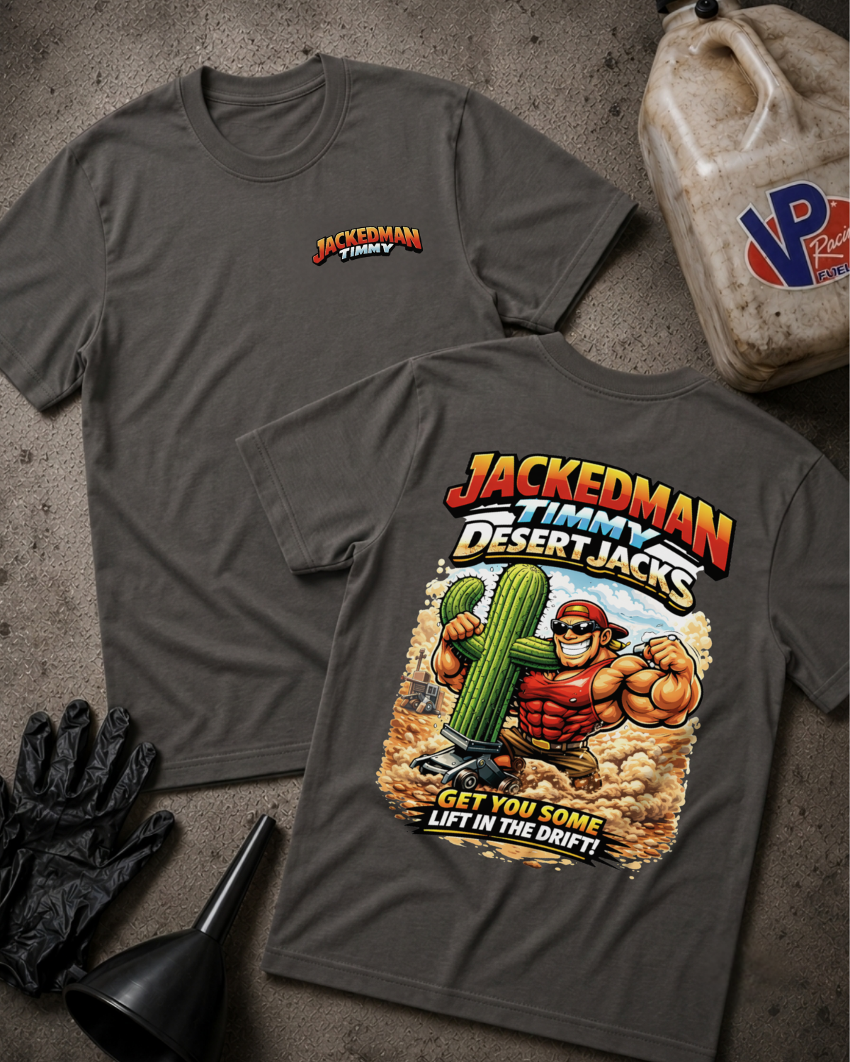 Two dark gray graphic t-shirts displayed flat on a textured concrete surface, showing both the front chest logo and the back large graphic print for 'Jackedman Team Desert Jacks'. The scene is styled with black gloves, a black funnel, and a plastic fuel jug.