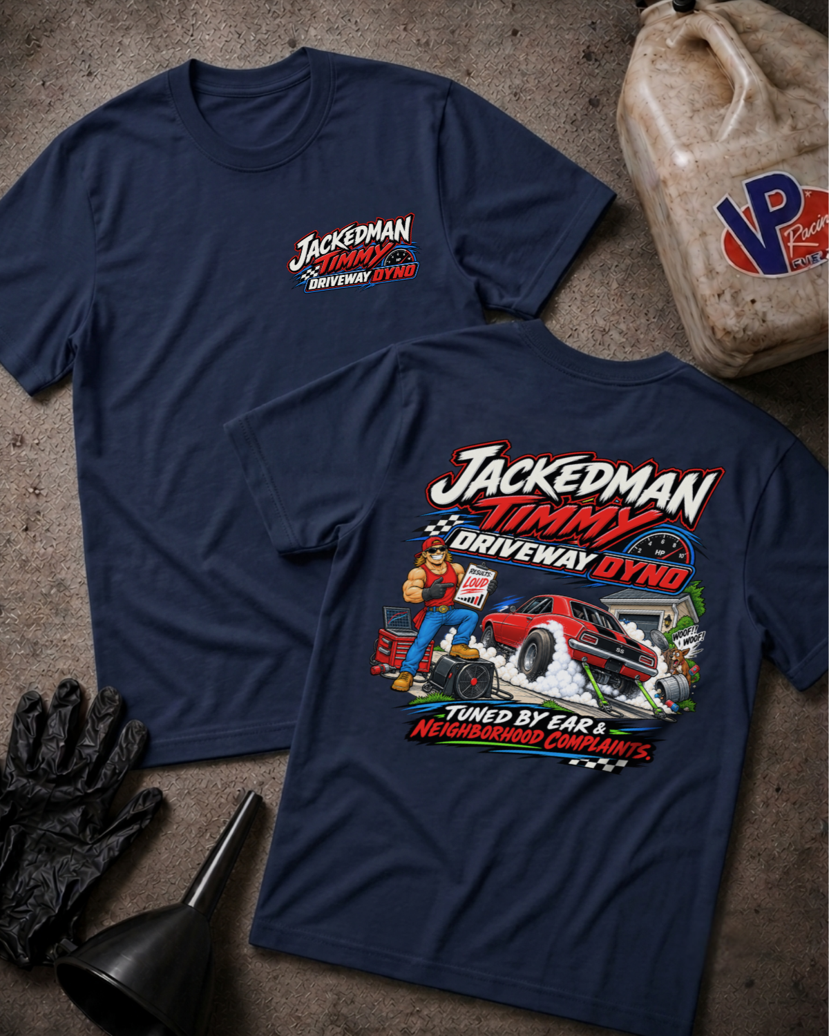 Two navy blue t-shirts displayed flat on a textured gray surface, showing the front and back graphics for 'Jackedman Timmy Driveway Dyno'. The front features a small white and red logo on the left chest, while the back features a large, colorful graphic of a race car, a person in a jumpsuit, and garage tools.