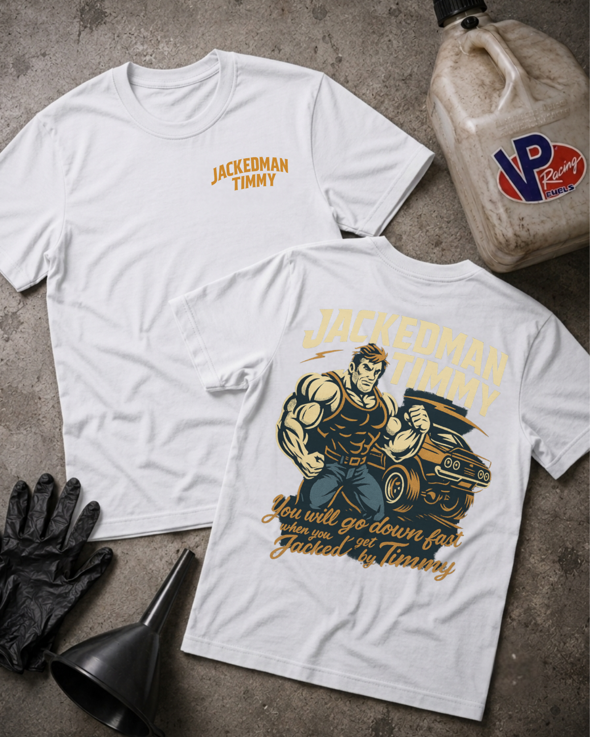 Two white graphic T-shirts laid flat on a gray concrete-style surface, with a black funnel, black gloves, and a plastic jug nearby. The front shirt has a small gold 'Jackedman Timmy' logo on the chest, and the back shirt has a large vintage-style illustration of a muscular man next to a car with the same gold and dark blue text.