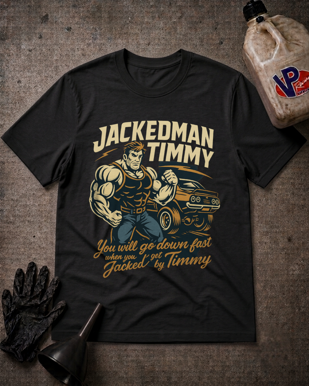 A black graphic t-shirt featuring a muscular man flexing next to a muscle car with the text 'JACKEDMAN TIMMY' and 'You will go down fast when you get Jacked by Timmy'. The shirt is displayed in a flat-lay arrangement on a textured gray background, accompanied by a black oil pan, black gloves, and a plastic jug of oil.