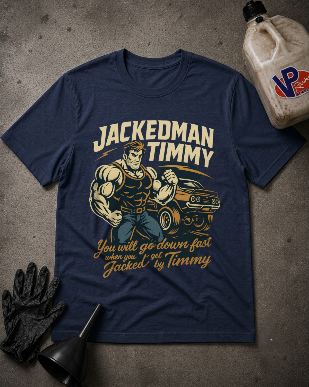 A navy blue graphic t-shirt featuring a muscular man flexing next to a muscle car with the text 'JACKEDMAN TIMMY' and 'You will go down fast when you get Jacked by Timmy'. The shirt is displayed in a flat-lay arrangement on a gray concrete floor with a black oil change funnel, a black glove, and a plastic jug of VP Brand motor oil.