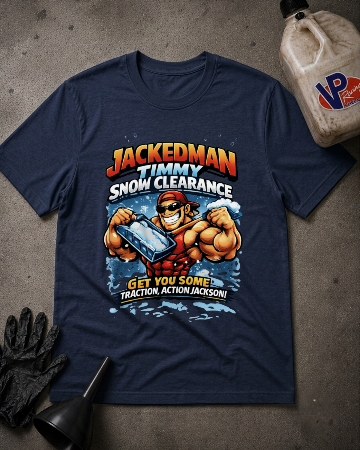 A navy blue graphic t-shirt featuring a cartoon illustration of a muscular man clearing snow, with the text 'JACKEDMAN TIMMY SNOW CLEARANCE' and 'GET YOU SOME Traction, ACTION, JACKSON!'. The t-shirt is displayed in a flat-lay arrangement on a gray concrete-like surface, accompanied by a black work glove, a black funnel, and a plastic jug in the background.