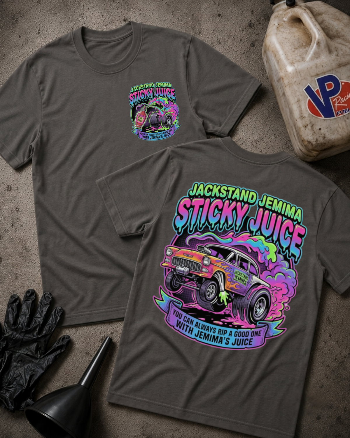 Two dark gray graphic T-shirts laid flat on a textured concrete surface, showing the front and back designs. The shirts feature a colorful truck graphic with the text 'Jackstand Jemima Sticky Juice.