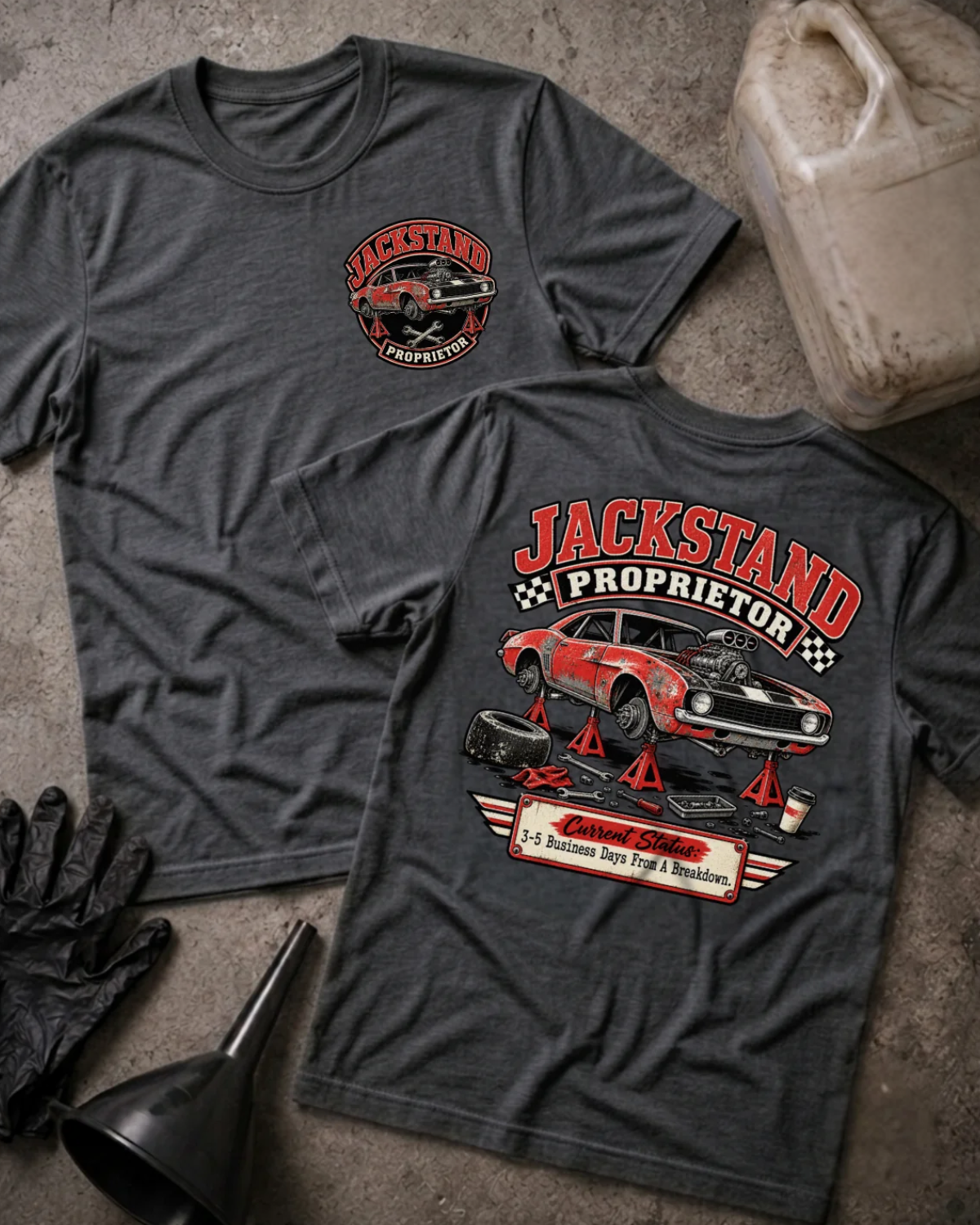 Front and back of Jackstand Proprietor dark grey heather T-shirt with chest logo, weathered red muscle car on jack stands, and “Current status: 3–5 business days from a breakdown” slogan.