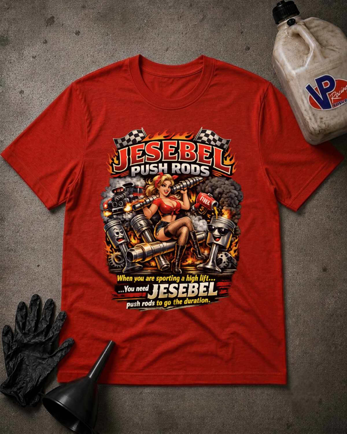 A red graphic t-shirt laid flat on a gray concrete-like surface, surrounded by black gloves, a black funnel, and a plastic jug. The shirt features a large vintage-style chest graphic with the text 'JESEBEL PUSH RODS' and 'push rods to go the duration.