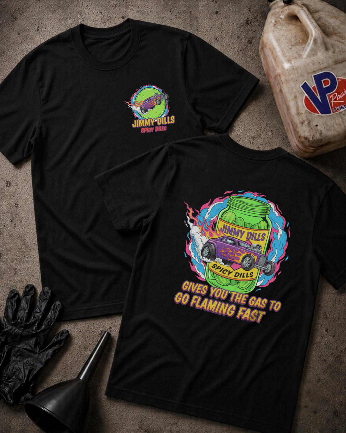 Two black graphic T-shirts laid flat on a textured gray surface, showing both front and back designs. The shirts feature a colorful circular 'Jumpy Dills Spicy Dills' graphic with a purple car and the phrase 'GIVES YOU THE GAS TO GO FLAMING FAST.