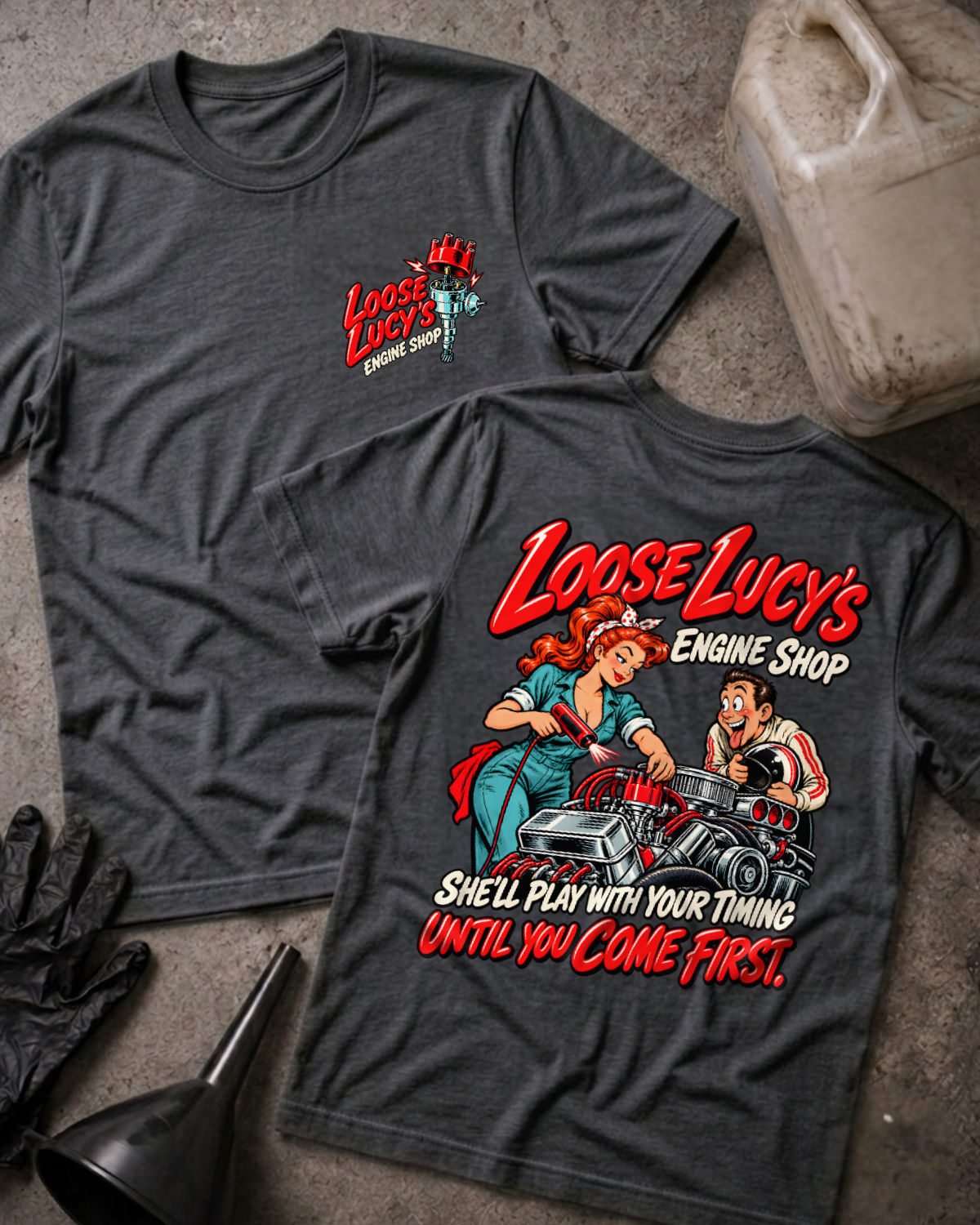 Dark grey heather Loose Lucy’s Engine Shop T-shirt showing the front chest logo and back cartoon of a woman mechanic timing a hot rod engine with a timing light, “She’ll Play With Your Timing Until You Come First,” with gloves, funnel, and oil jug props.