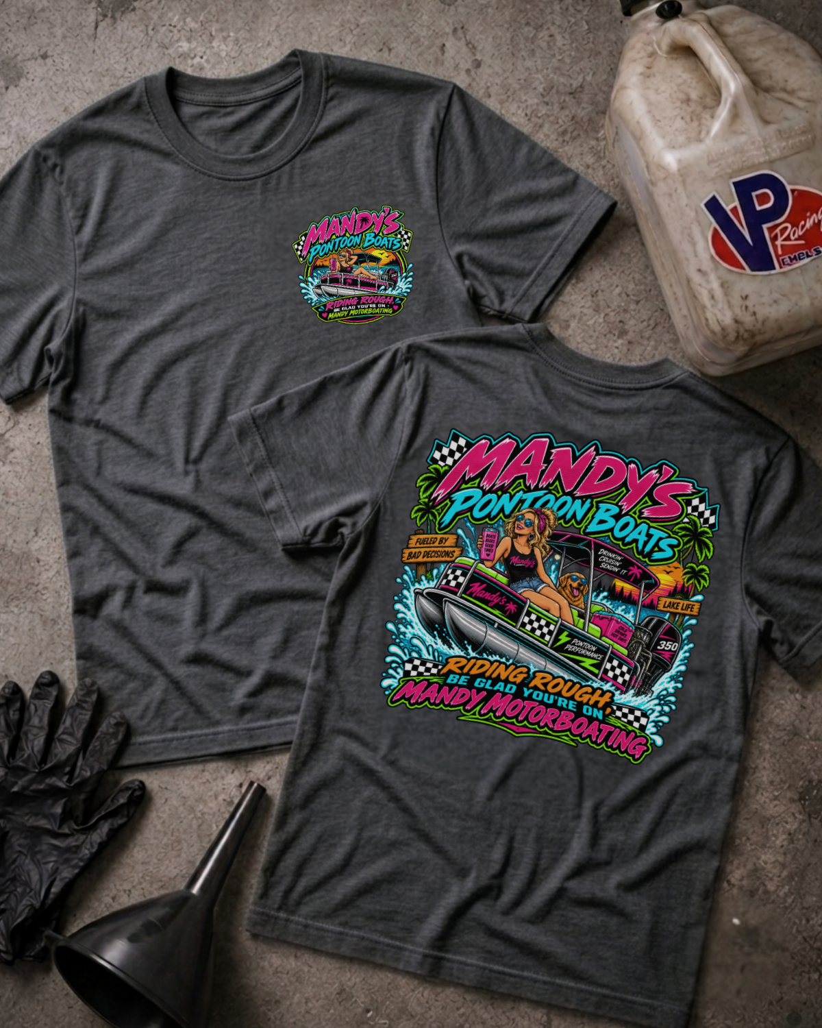 Two dark heather gray t-shirts displayed flat on a concrete surface, showing the front and back designs. The front features a small colorful chest graphic, while the back features a large, vibrant graphic for 'Mandy's Pontoon Boats Riding Rough Be Glad You're On Mandy Motorboating'.