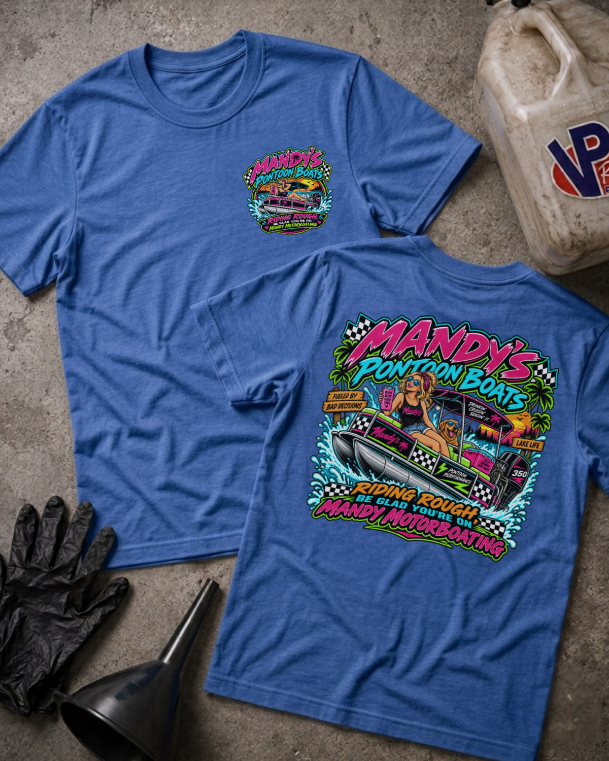 Two heather blue graphic T-shirts laid flat on a concrete-like surface, showing the front and back designs. The shirts feature a colorful 'Mandy's Pontoon Boats' graphic with a race pontoon boat, palm trees, and bold text.
