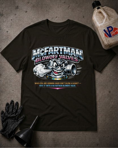 A black graphic t-shirt featuring a McFartman Blowoff Valve cartoon mascot and text, styled in a flat-lay with a oil jug, black gloves, and a funnel on a textured gray concrete background.