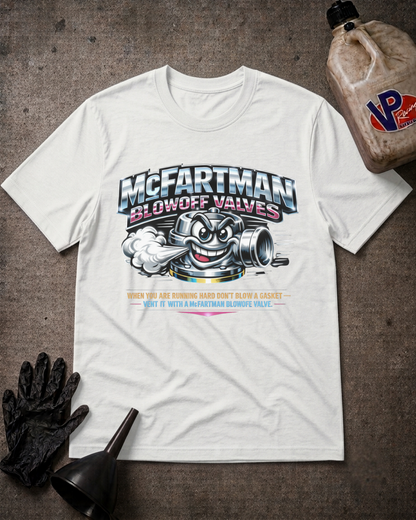 A white graphic t-shirt featuring a cartoon engine mascot and the text 'McFartman Blowff Valves' laid flat on a dark textured surface with black gloves, a funnel, and a VP fuel bottle as props.