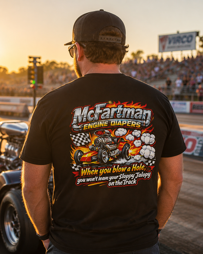Back view of a man wearing a black Bella+Canvas 3001 McFartman Engine Diapers drag racing t-shirt at a drag race during golden hour. Large back graphic shows a blown drag car with flames, smoke clouds, checkered flags, and humorous racing text. High-detail motorsports lifestyle mockup with authentic track atmosphere and sunset lighting.
