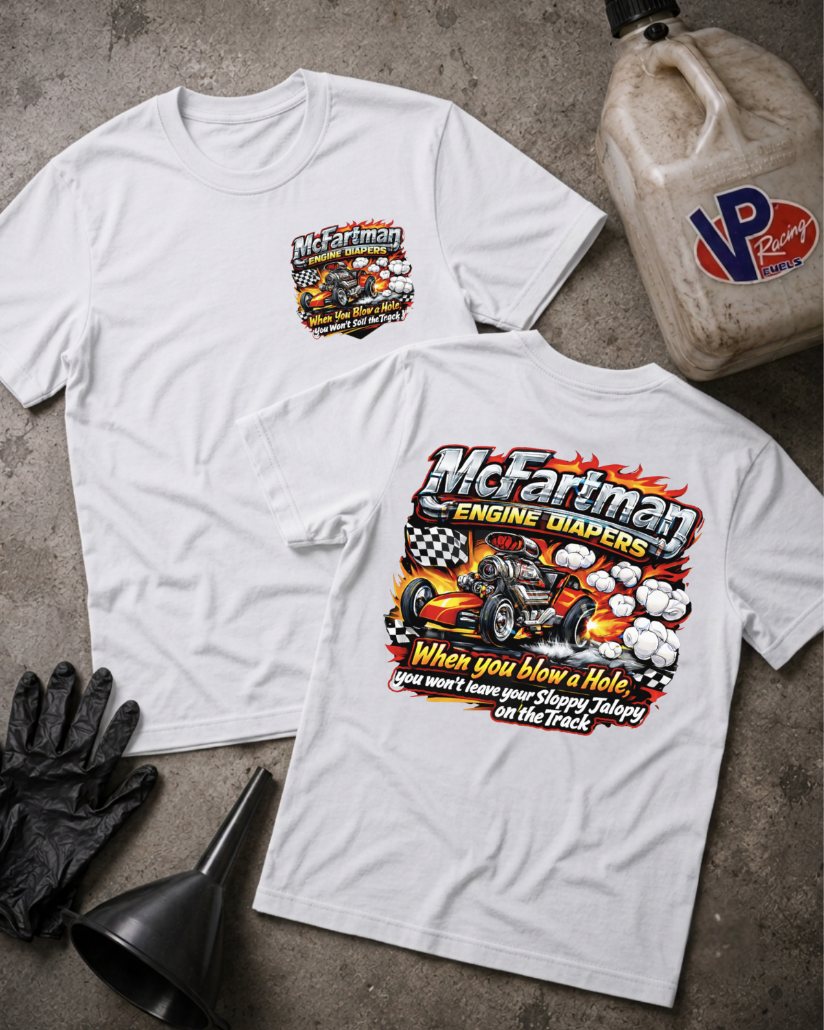 Two white graphic t-shirts displayed flat on a gray concrete surface, with a black funnel, black gloves, and a plastic jug of VP Racing props. The front shirt shows a small chest graphic, and the back shirt shows a large graphic of a race car with the text 'McFartman ENGINE DIABERS' and 'When you blow a Hole you won't have your Sloppy Jalopy on the Track'
