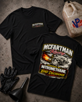 Two black graphic t-shirts laid flat on a textured gray surface, surrounded by racing-themed props including black gloves, a funnel, and a plastic jug. The front shirt shows a small chest logo, and the back shirt features a large graphic with the text 'McFartman Racing' and 'Powered by Nitromethane Bad Decisions' with an engine illustration.