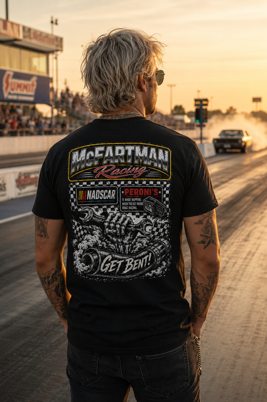 Rear view of man wearing a black McFartman Racing “Get Bent!” drag racing t-shirt at a drag strip during golden hour with burnout smoke, staging lanes, and gritty motorsports atmosphere.