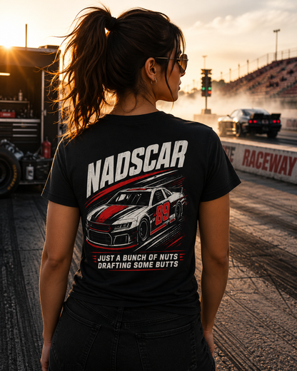 Person wearing a black t-shirt with NADSCAR graphics and 'NADSCAR JUST A BUNCH OF NUTS DRAFTING SOME BUTTS' text at a race track.