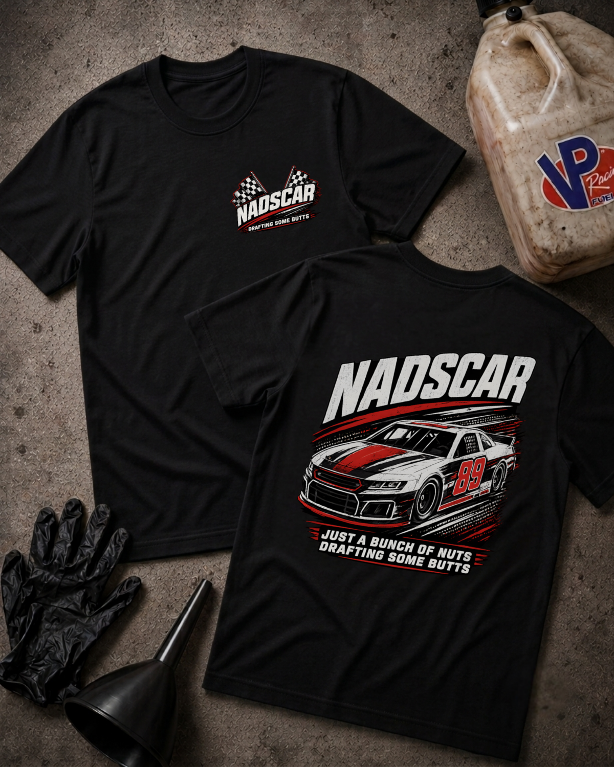 Two black short-sleeve T-shirts laid flat on a textured gray surface, one showing a small white and red NADSCAR chest logo and the other showing a large back graphic with a NADSCAR race car and the text 'NADSCAR' and 'JUST A BUNCH OF NUTS DRAFTING SOME BUTTS.' Black gloves and a funnel sit at the lower left, and a worn plastic jug with a VP logo sits at the upper right.