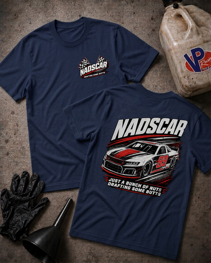 Two navy blue t-shirts with NADSCAR graphics, displayed in a flat-lay arrangement with black gloves, a funnel, and a plastic jug on a textured concrete surface.