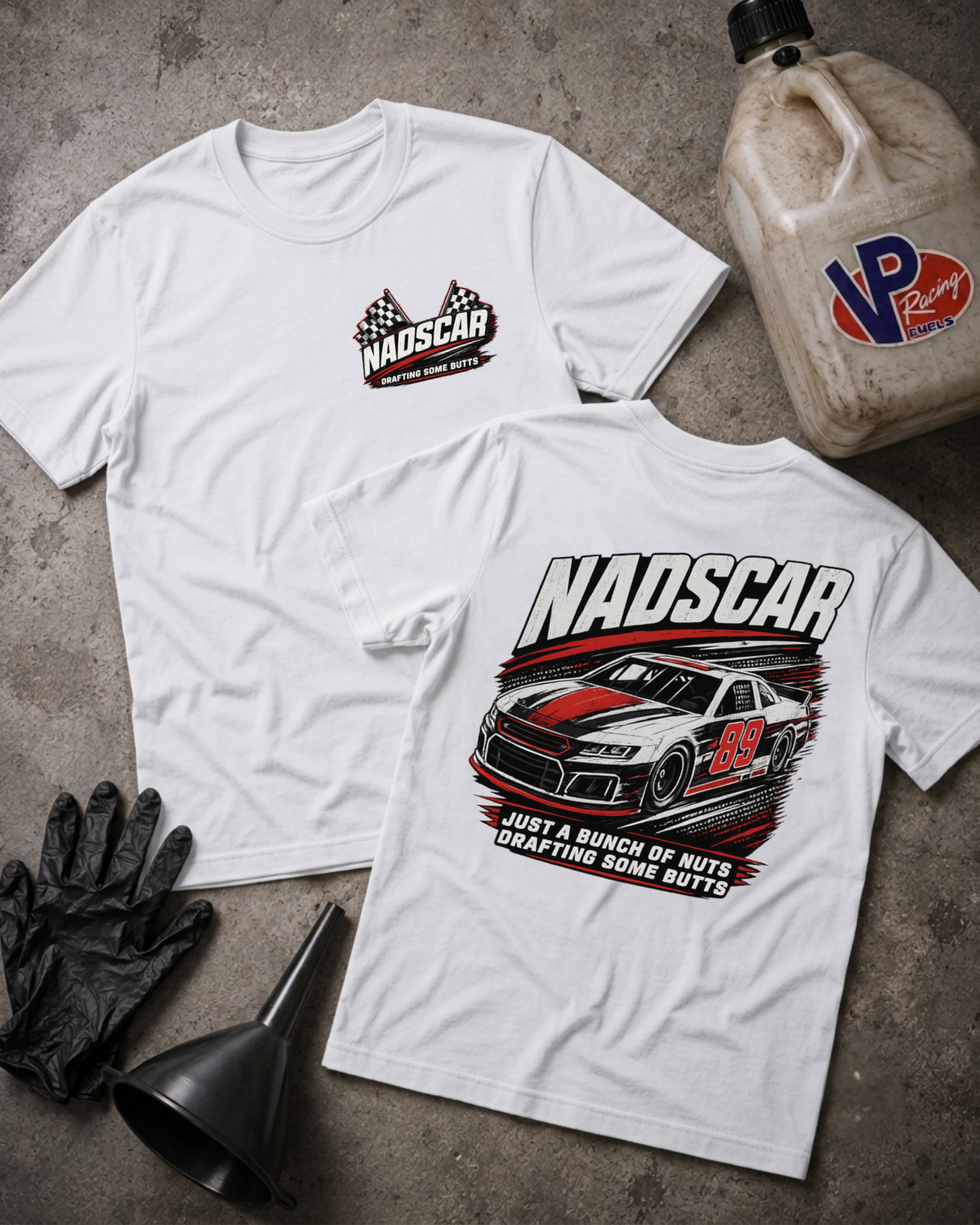 Two white graphic t-shirts displayed flat on a gray concrete surface, with a NADSCAR logo on the front and a large NADSCAR race car graphic on the back. Styled flat-lay props include a plastic jug, black gloves, and a funnel.