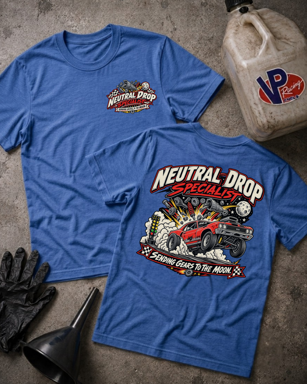 Two blue graphic T-shirts laid flat on a concrete surface, showing the front and back designs. The shirts feature the Neutral Drop branding with a small chest logo on the front and a large back graphic reading 'Neutral Drop Specialist' with a red race car and flames.