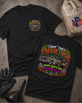 Two black graphic T-shirts laid flat on a textured concrete surface, with a black glove, funnel, and a worn plastic jerrycan nearby. The front shirt shows a small multicolor chest graphic, and the back shirt shows a large colorful truck graphic with the text 'Off the Trailer Trash' and 'Junk Hauling and Freeballin'.