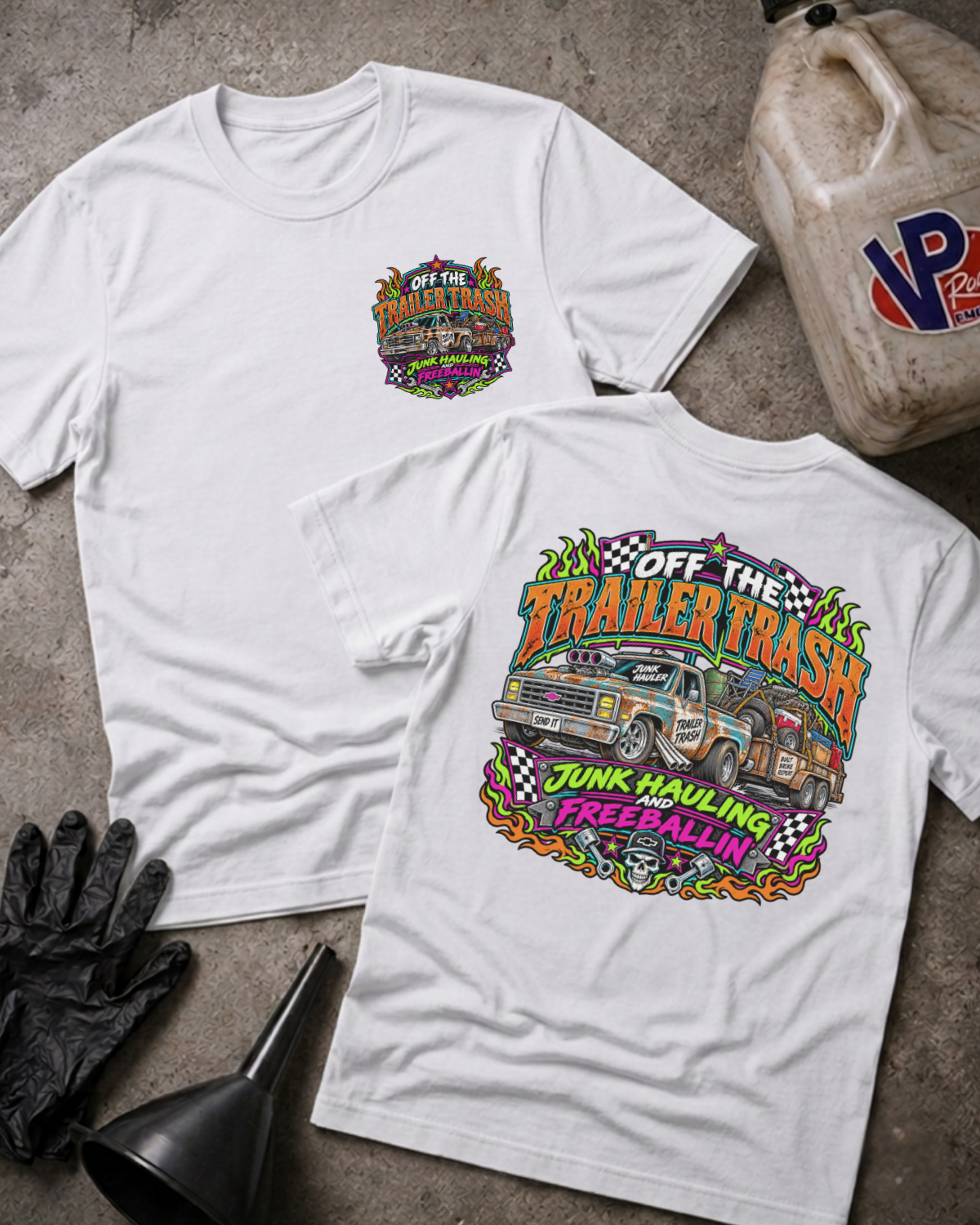 Two white graphic T-shirts shown on a concrete floor, with the front view on the left and the back view on the right. The back shirt features a large colorful truck-themed graphic with the text 'Off The Trailer Trash' and 'Junk Hualing and Free Ballin''.