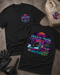 Two black graphic T-shirts laid flat on a textured gray surface, with a vintage-style neon race car print on the back of one shirt and a smaller circular chest print on the other. Props include black gloves, a funnel, a plastic jug, and a worn work hat.