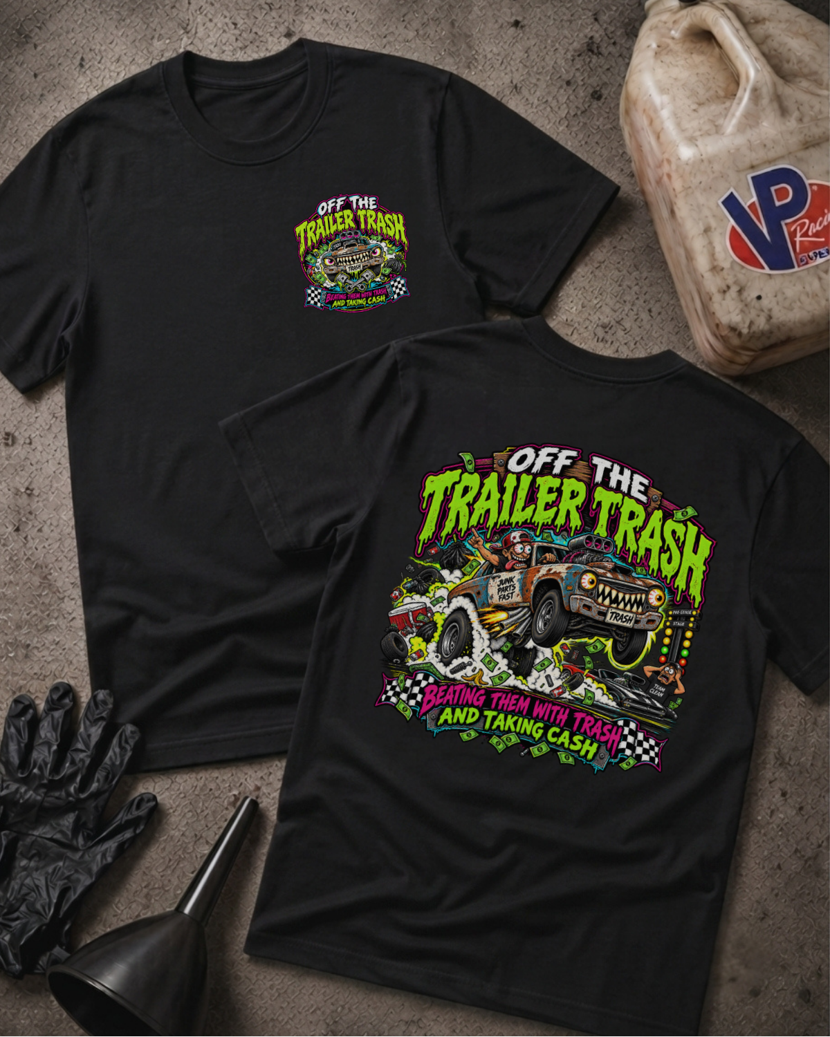 Two black graphic T-shirts laid flat on a textured gray surface, showing the front and back designs. The shirts feature a colorful truck illustration with the text 'OFF THE TRAILER TRASH' and 'BEATING THEM WITH TRASH AND TAKING CASH.