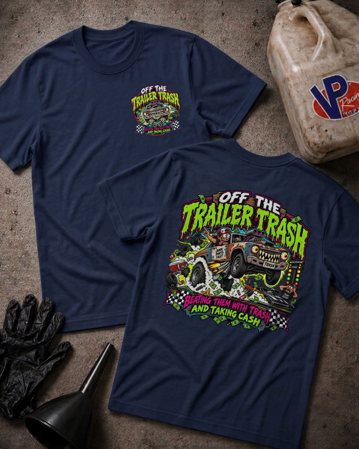 Two navy blue graphic t-shirts displayed on a textured concrete surface with a gas bottle, black gloves, and a funnel as props. The front shirt shows a small chest graphic, while the back shirt features a large colorful graphic with the text 'OFF THE TRAILER TRASH'.