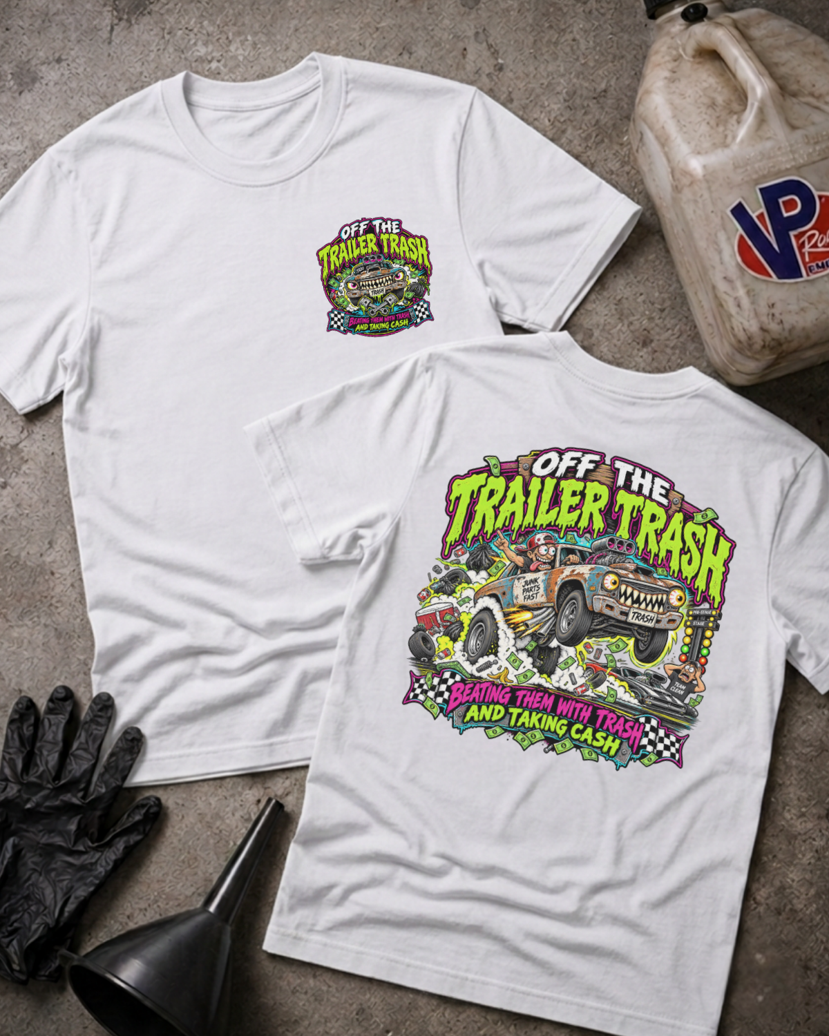 Two white graphic t-shirts displayed on a textured concrete surface with a gas bottle, black gloves, and a funnel as props. The front shirt shows a small chest graphic, while the back shirt features a large colorful graphic with the text 'OFF THE TRAILER TRASH'.