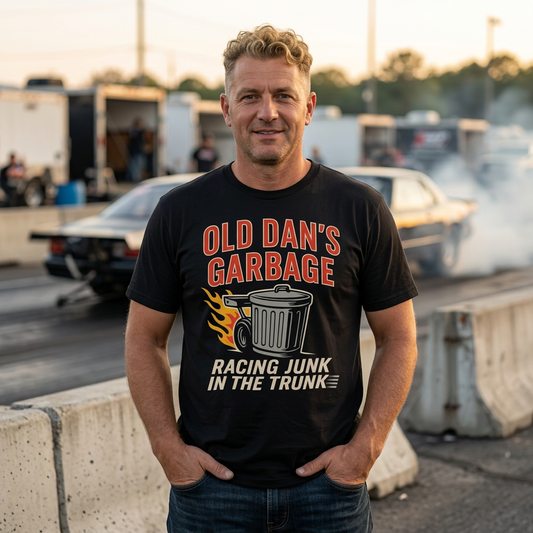 Man wearing a black t-shirt with 'Old Dan's Garbage' graphic at a race track.