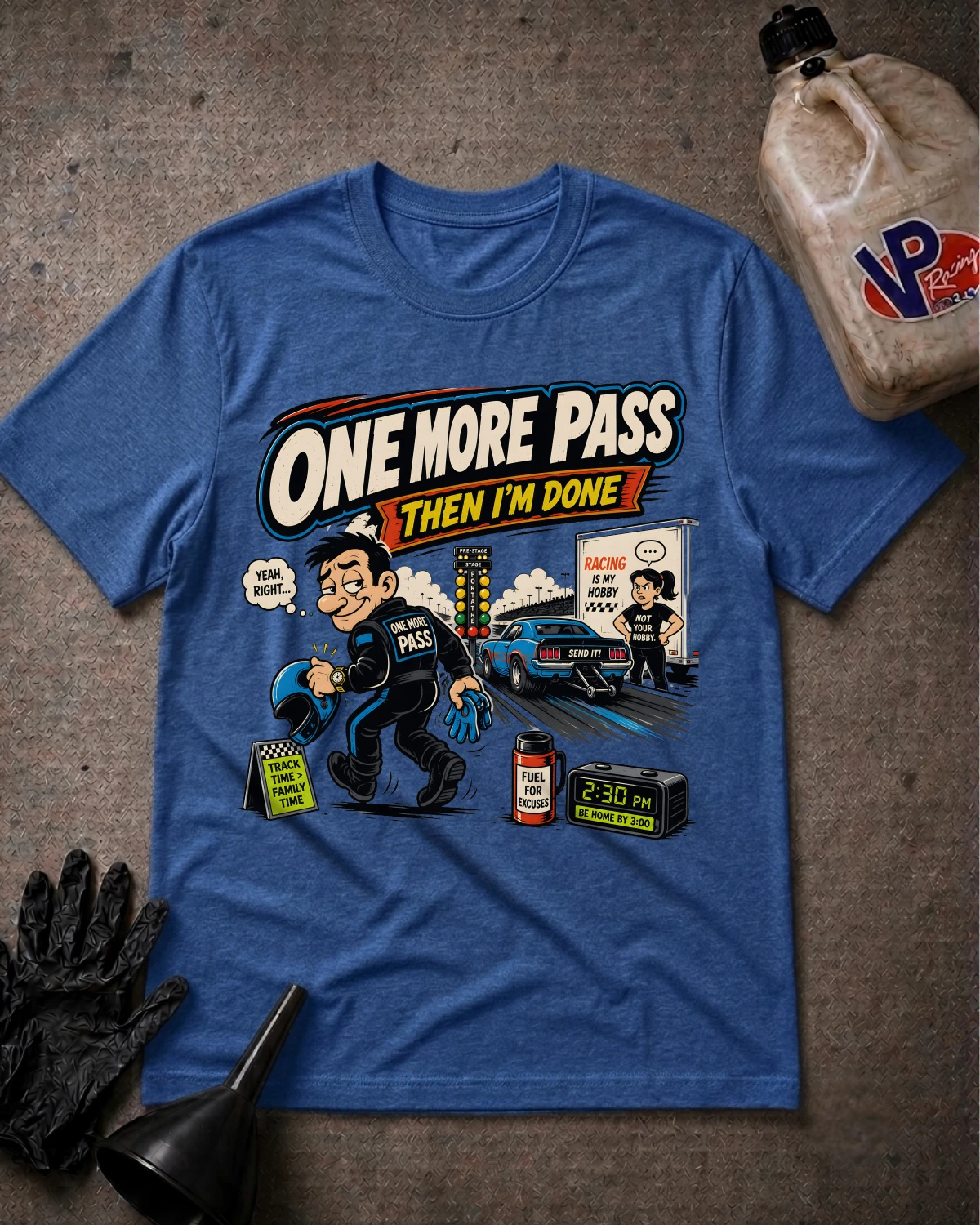 A heather blue graphic t-shirt featuring a cartoon of a race car driver with the text 'ONE MORE PASS THEN I'M DONE'. The shirt is displayed in a flat-lay arrangement on a textured gray surface, surrounded by racing-themed props including a black glove, a funnel, and a fuel jug.