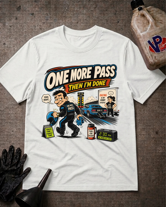 A white graphic t-shirt laid flat on a textured gray surface, featuring a cartoon illustration of a police officer taking a test with the text 'ONE MORE PASS THEN I'M DONE'. A black oil can, black gloves, and a funnel are arranged around the shirt as props.