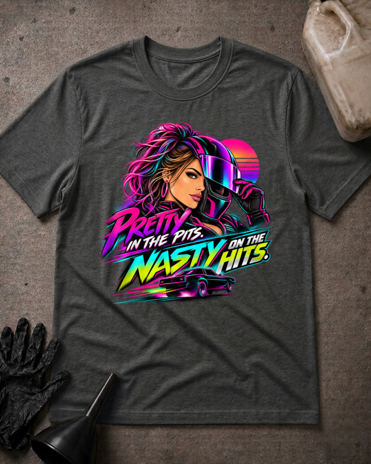 Dark grey heather T-shirt laid flat with a neon woman racer, racing helmet, muscle car and sunset graphic reading “Pretty in the Pits. Nasty on the Hits.”