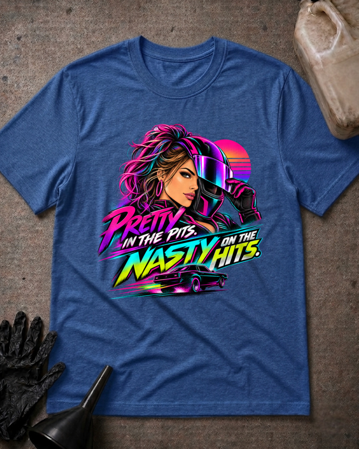 Heather true royal blue T-shirt laid flat with a neon woman racer, racing helmet, muscle car and sunset graphic reading “Pretty in the Pits. Nasty on the Hits.”