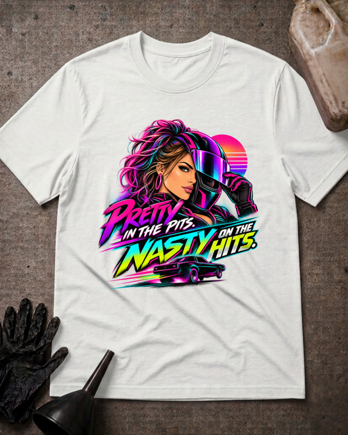 White T-shirt laid flat with a neon woman racer, racing helmet, muscle car and sunset graphic reading “Pretty in the Pits. Nasty on the Hits.”